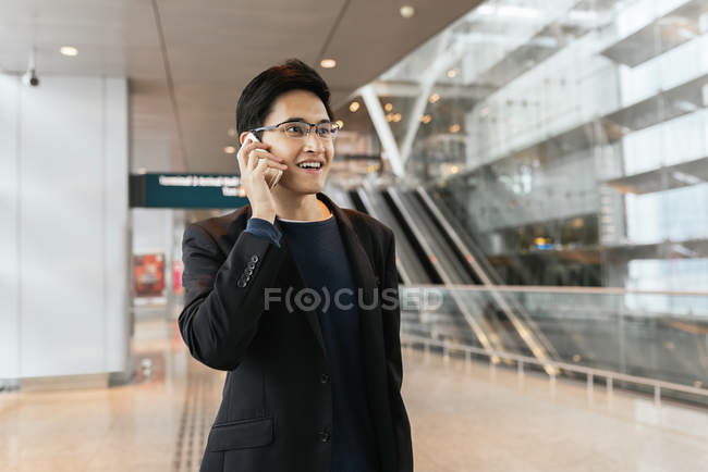 Young asian businessman with luggage and smartphone in airport — Stock Photo