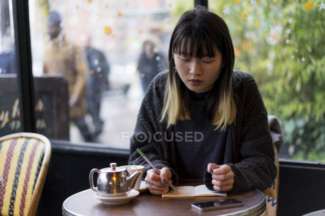Молода приваблива випадкова азіатська жінка пише нотатки в кафе — стокове фото