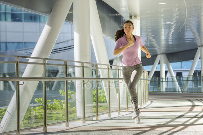 Una joven asiática está corriendo por la ciudad de Singapur por la mañana temprano. Pasa por una sección de arquitectura de acero y vidrio . - foto de stock