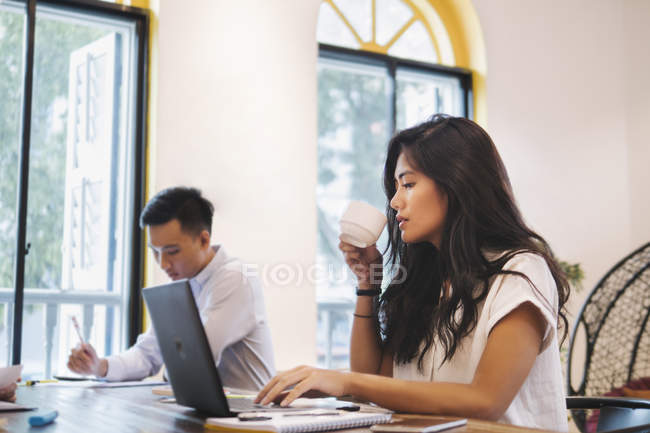 Молода азіатська жінка працює з ноутбуком в творчому сучасному офісі — стокове фото