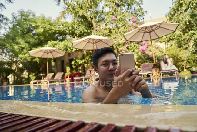 Молодий чоловік фотографує зі своїм мобільним телефоном у басейні — стокове фото