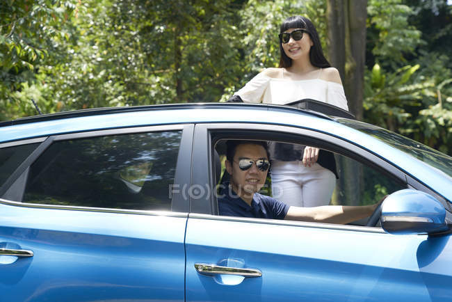 Couple standing through the sun roof of a car — Stock Photo