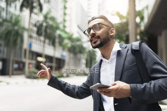 Young successful businessman using smartphone and catching cab — Stock Photo