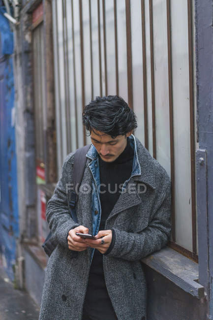 Молодий привабливий випадковий азіатський чоловік використовує смартфон на відкритому повітрі — стокове фото