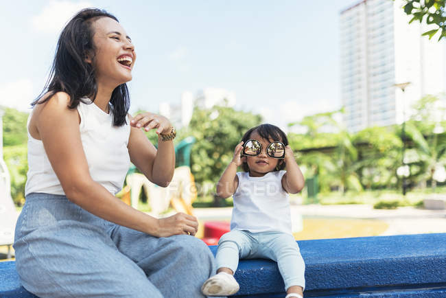 Joven madre con asiático hija tener divertido en parque infantil - foto de stock