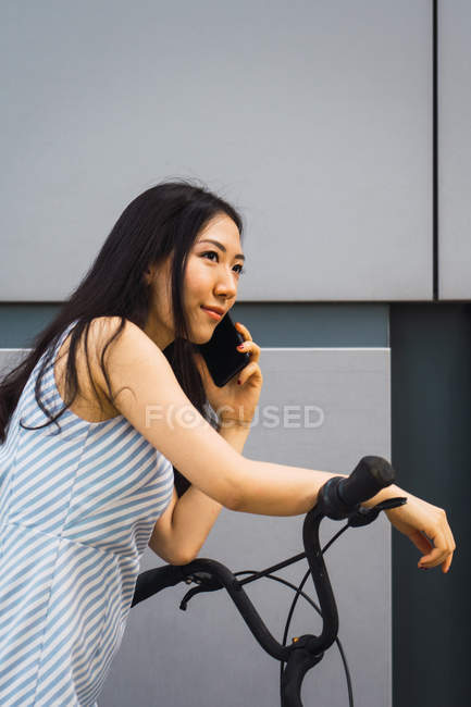 Joven asiático mujer con bicicleta usando smartphone - foto de stock