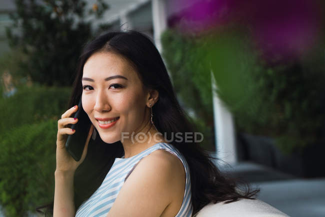 Молода азіатська жінка використовує смартфон і дивиться на камеру — стокове фото
