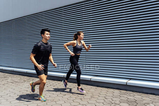 Asian couple running against wall — Stock Photo