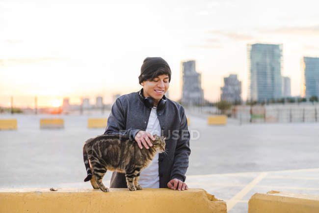 Joven asiático millennial disfrutando el atardecer y acariciando gato - foto de stock