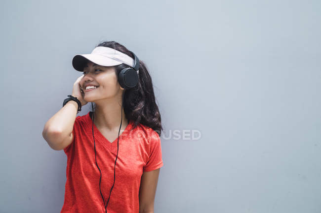 Junge asiatische sportliche Frau mit Kopfhörern gegen graue Wand — Stockfoto