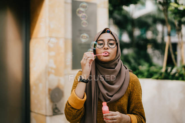 Молодая азиатская мусульманка в хиджабе делает пузыри — стоковое фото