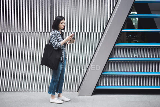 Giovane bella ragazza asiatica in abiti casual utilizzando smartphone sulle strade della città — Foto stock