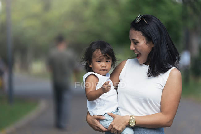 Joven madre con asiático hija contra borrosa fondo - foto de stock