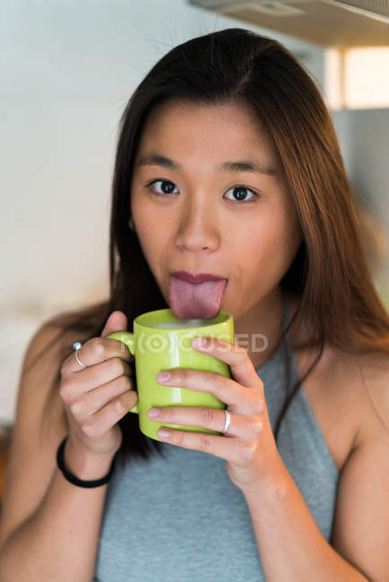 Молода приваблива азіатська жінка показує язик і тримає чашку кави — стокове фото