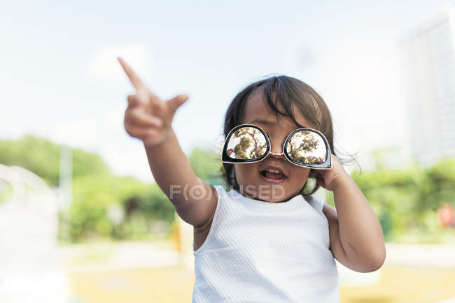 Cute little asian girl in sunglasses against blurred background — Stock Photo