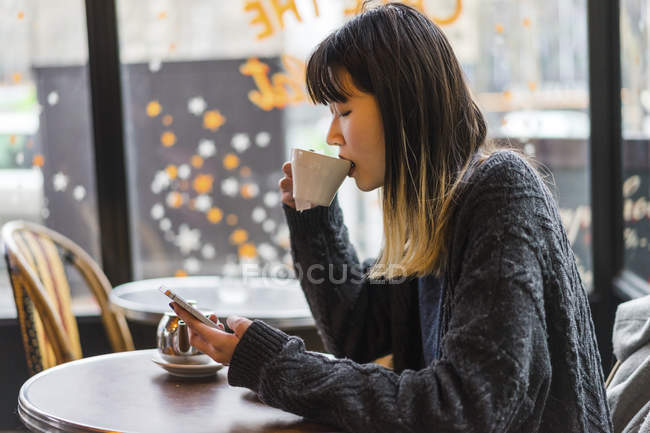 Joven atractivo casual asiático mujer bebiendo café en café - foto de stock