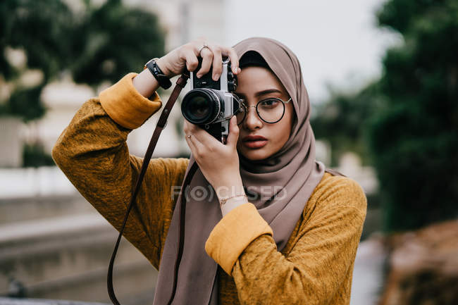 Joven asiático musulmán mujer en hijab tomando foto con cámara - foto de stock