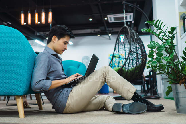 Молодой азиатский бизнесмен, использующий ноутбук в современном офисе — стоковое фото