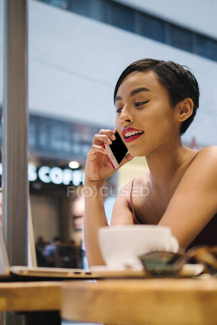 Medio retrato de una joven malaya singapurense usando su teléfono en un café mientras trabajaba . - foto de stock