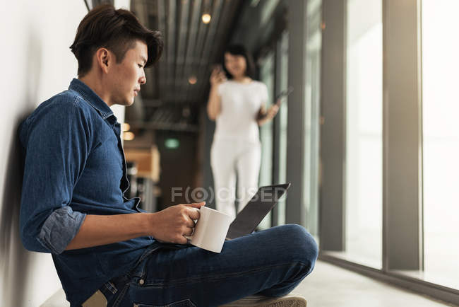 Two young asian people at work with laptop in modern office — Stock Photo