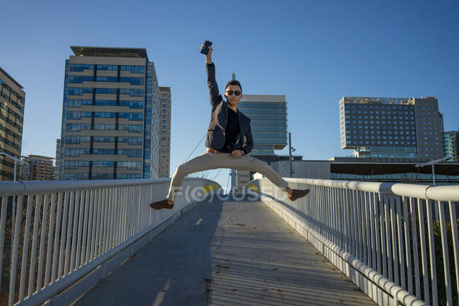 Молодий азіатський чоловік стрибає в повітрі зі смартфоном — стокове фото