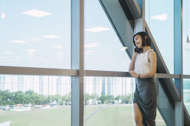Jovem asiático mulher de negócios falando no smartphone no escritório moderno — Fotografia de Stock
