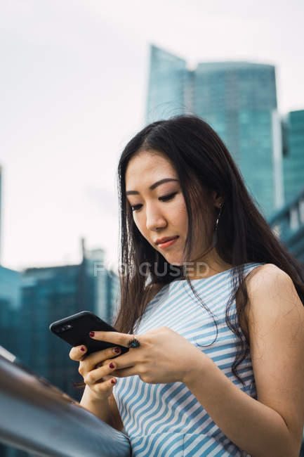 Молода азіатка використовує смартфон проти хмарочосів — стокове фото