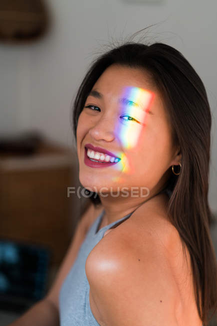 Portrait of young attractive asian woman with rainbow sunbeam on face — Stock Photo