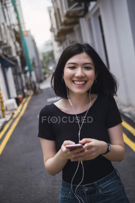 Jovem bela menina asiática em roupas casuais usando smartphone nas ruas da cidade — Fotografia de Stock