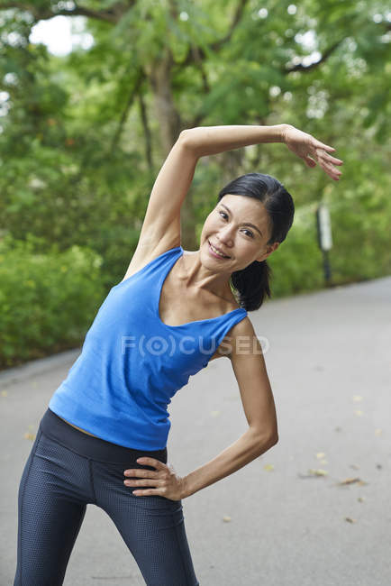 Frau mittleren Alters wärmt sich vor ihrem Lauf in botanischem Garten auf — Stockfoto