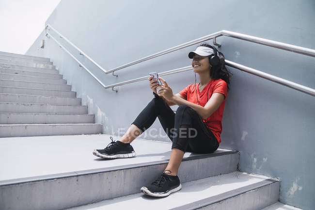 Junge asiatische sportliche Frau mit Kopfhörern und smart auf der Treppe — Stockfoto