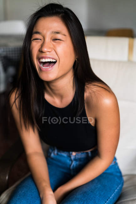 Junge attraktive asiatische Frau sitzt auf Sessel und lacht — Stockfoto