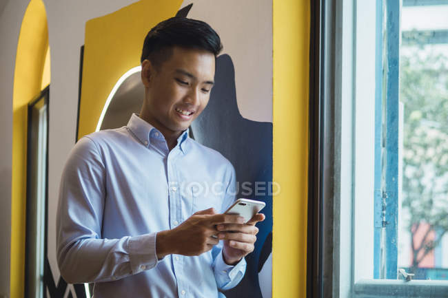 Giovane asiatico uomo utilizzando telefono in creativo moderno ufficio — Foto stock