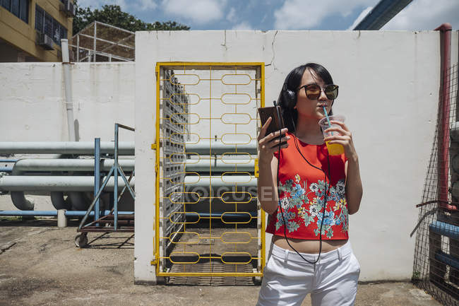 Asian woman with headphones and sunglasses against wall — Stock Photo