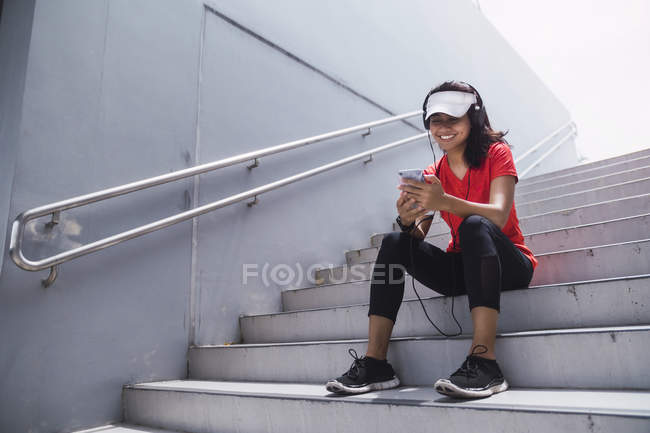 Jeune asiatique sportive femme à l'aide d'écouteurs et smart sur les escaliers — Photo de stock