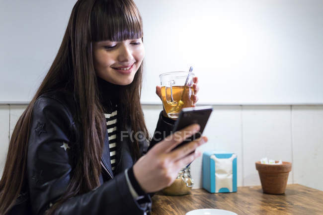 Молода жінка в кафе дивиться на її смартфон — стокове фото