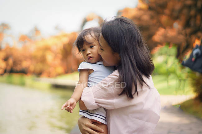 Cute asian mother and daughter kissing in park — Stock Photo