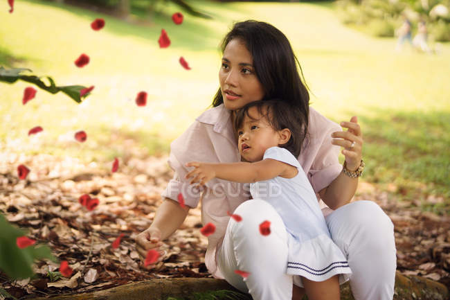 Lindo asiático madre y hija jugando con hojas en parque - foto de stock