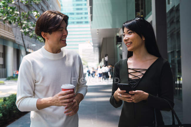 Молодая азиатская пара, идущая по улице со смартфоном и напитком — стоковое фото