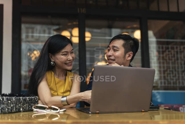 Happy young asian couple using laptop in cafe — Stock Photo