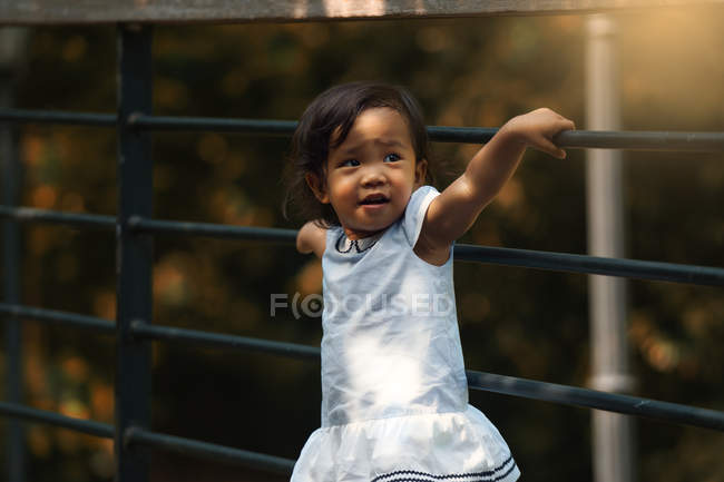 Poco lindo asiático chica al lado valla en parque - foto de stock