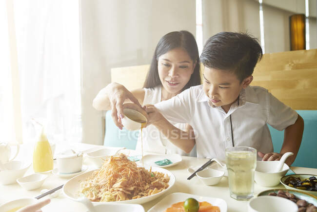 Щаслива азіатська сім'я разом в кафе, хлопчик наливає соус на локшину — стокове фото