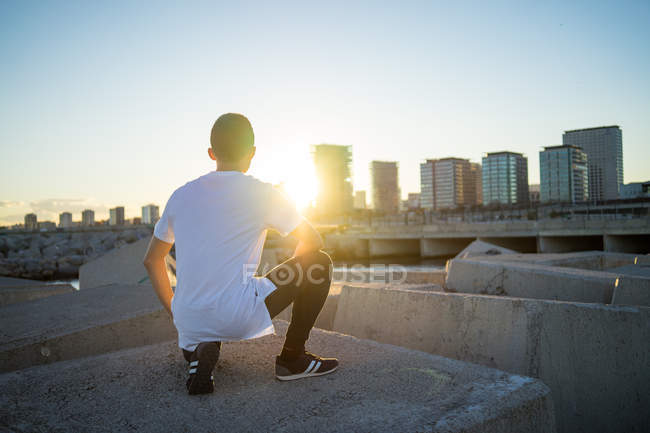 Vue arrière de jeune asiatique homme hunker vers le bas au coucher du soleil — Photo de stock