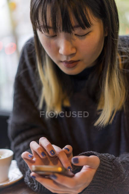 Молода приваблива випадкова азіатська жінка використовує смартфон у кафе — стокове фото