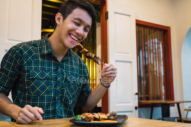 Giovane asiatico uomo mangiare kebab in confortevole bar — Foto stock