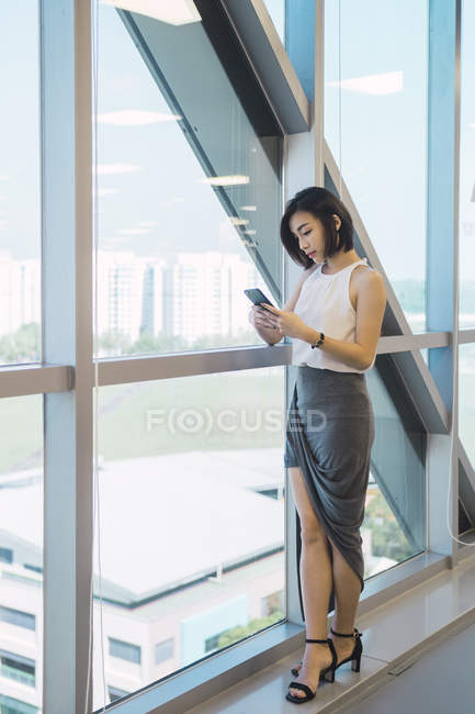 Giovane donna d'affari asiatica utilizzando smartphone in ufficio moderno — Foto stock