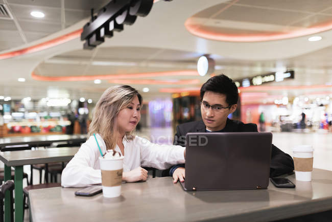 Young asian couple of businesspeople using laptop in airport — Stock Photo