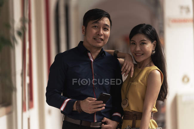 Glückliches junges asiatisches Paar, das sich umarmt und Smartphone benutzt — Stockfoto