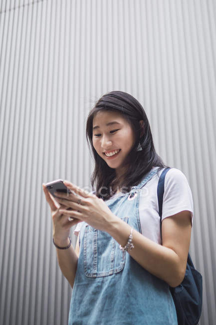 Молодий азіатський студент коледжу, використовуючи смартфон проти сірої стіни — стокове фото