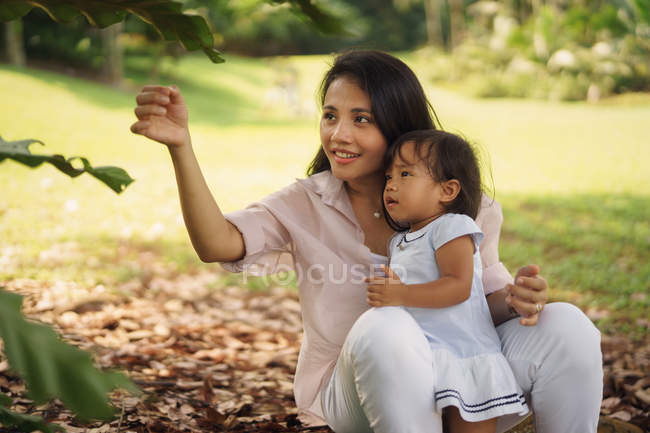 Cute asian mother and daughter playing with leaves in park — Stock Photo